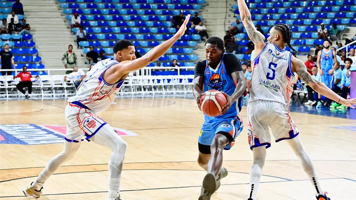 BJ Fiztgerald, del club San Lázaro, de mete en el medio de los defensas de San Lázaro, Ángel Núñez y Victor Liz.
