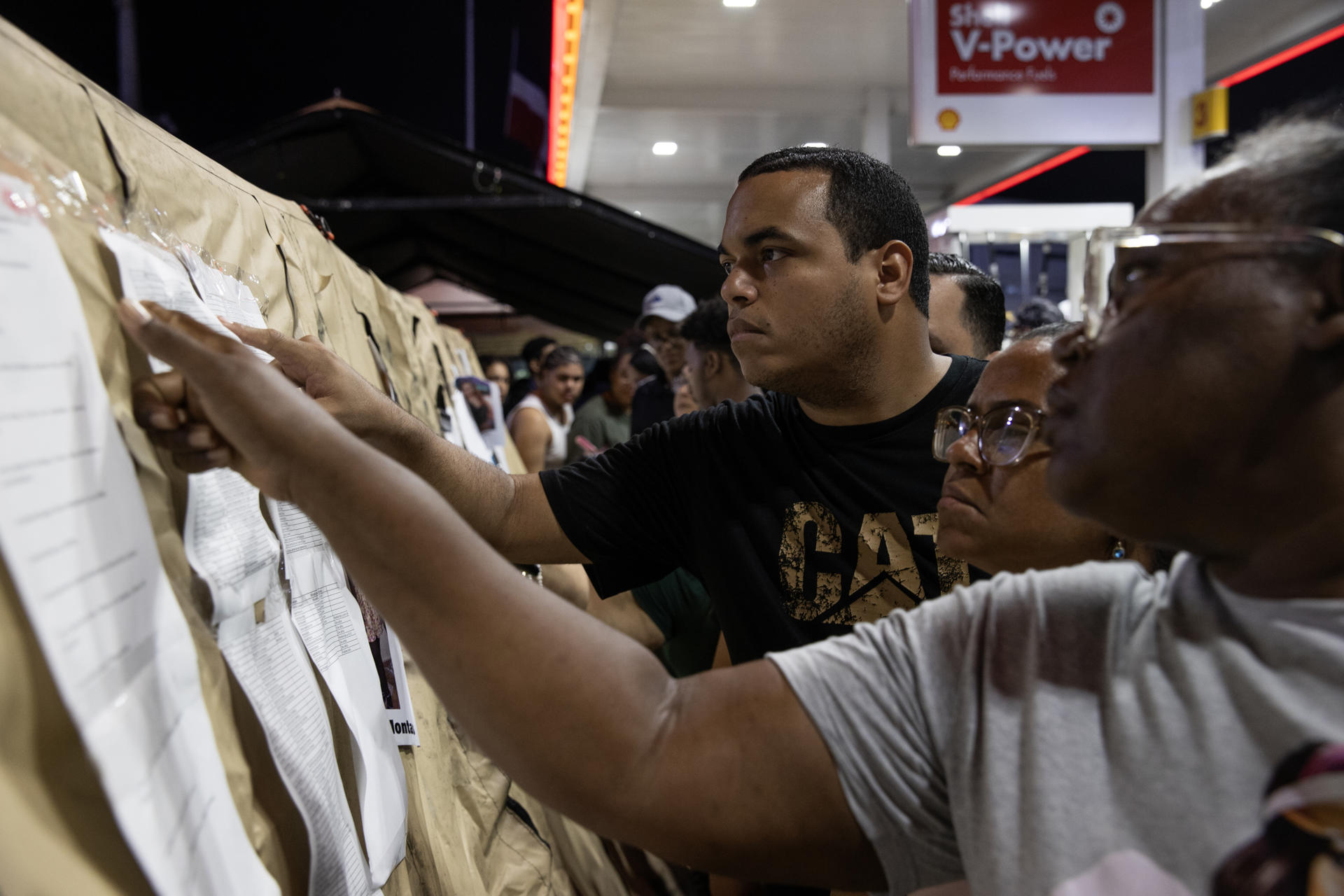 Personas observan papeles en panel informativo nocturno