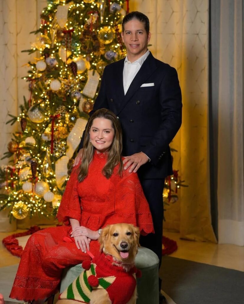 Pareja con perro frente a árbol de Navidad iluminado.