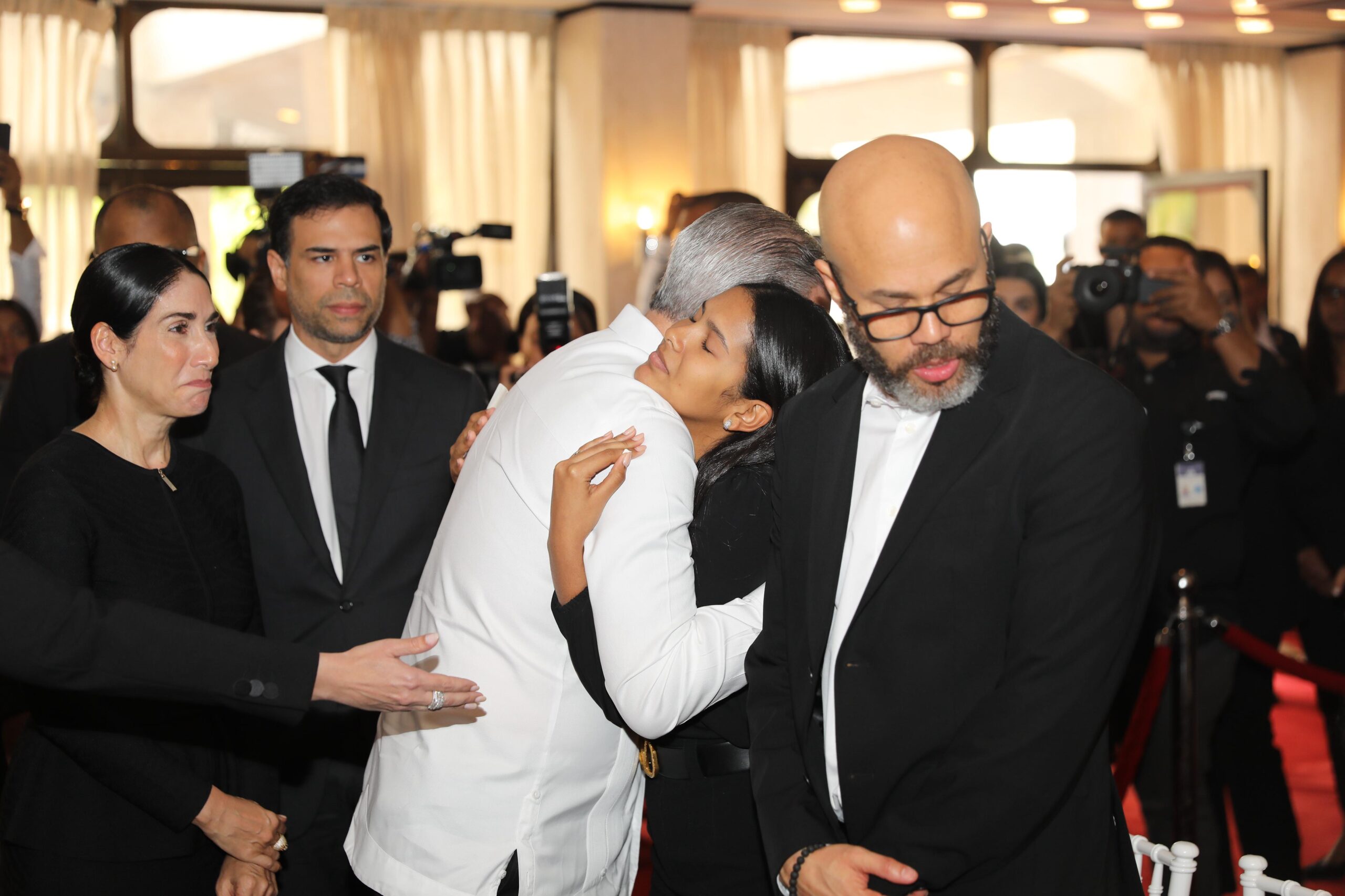 Personas abrazándose en evento formal con fotógrafos