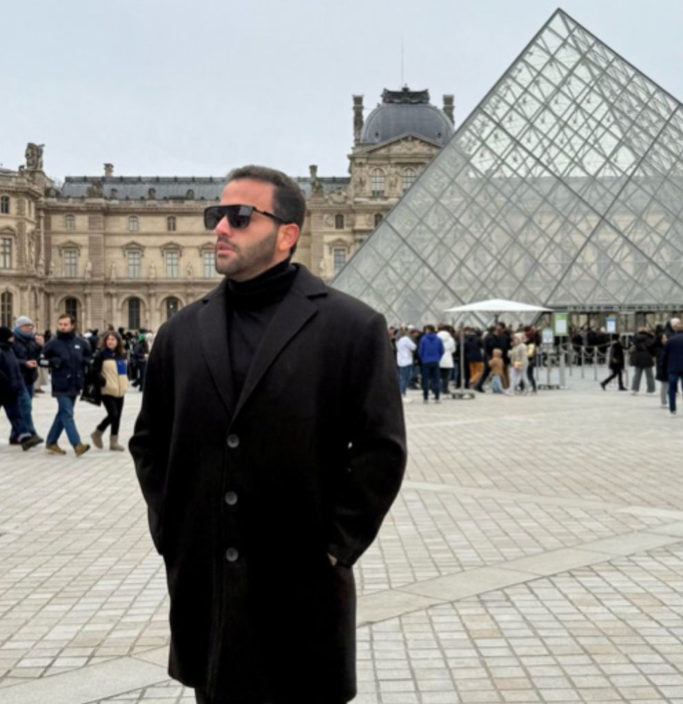 Hombre con abrigo frente a pirámide de cristal