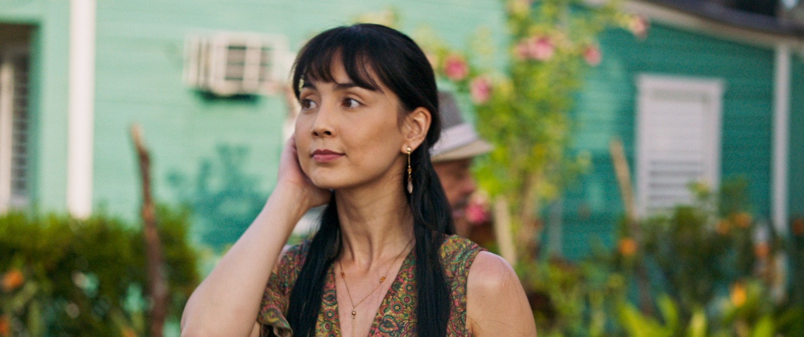 Mujer en jardín con casa verde de fondo.