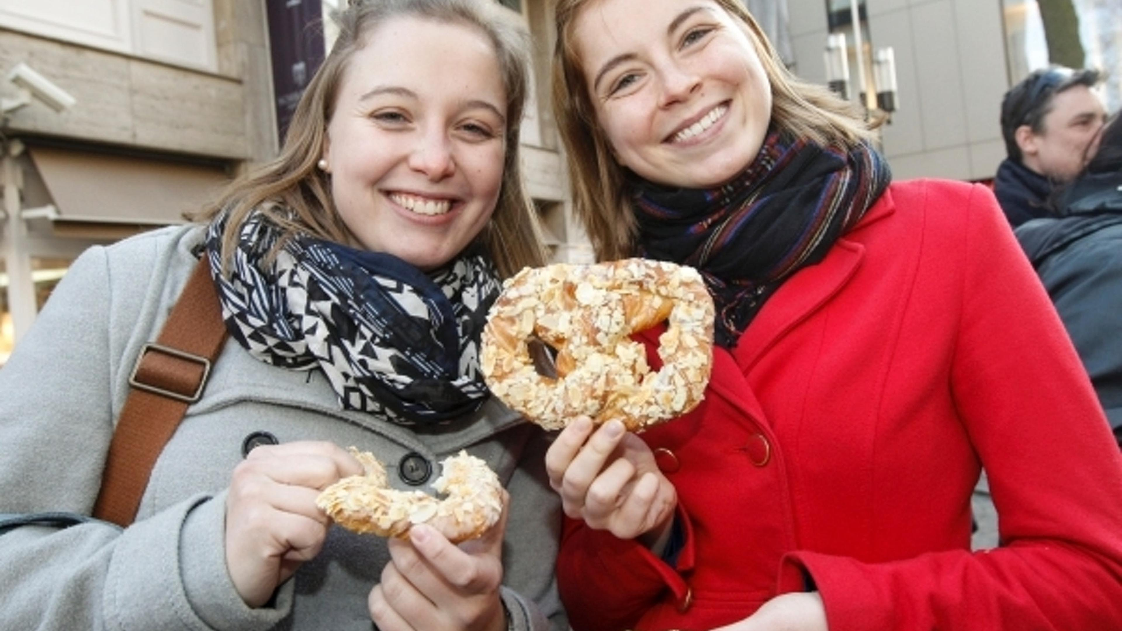 Dos personas sonríen con pretzels en la mano.