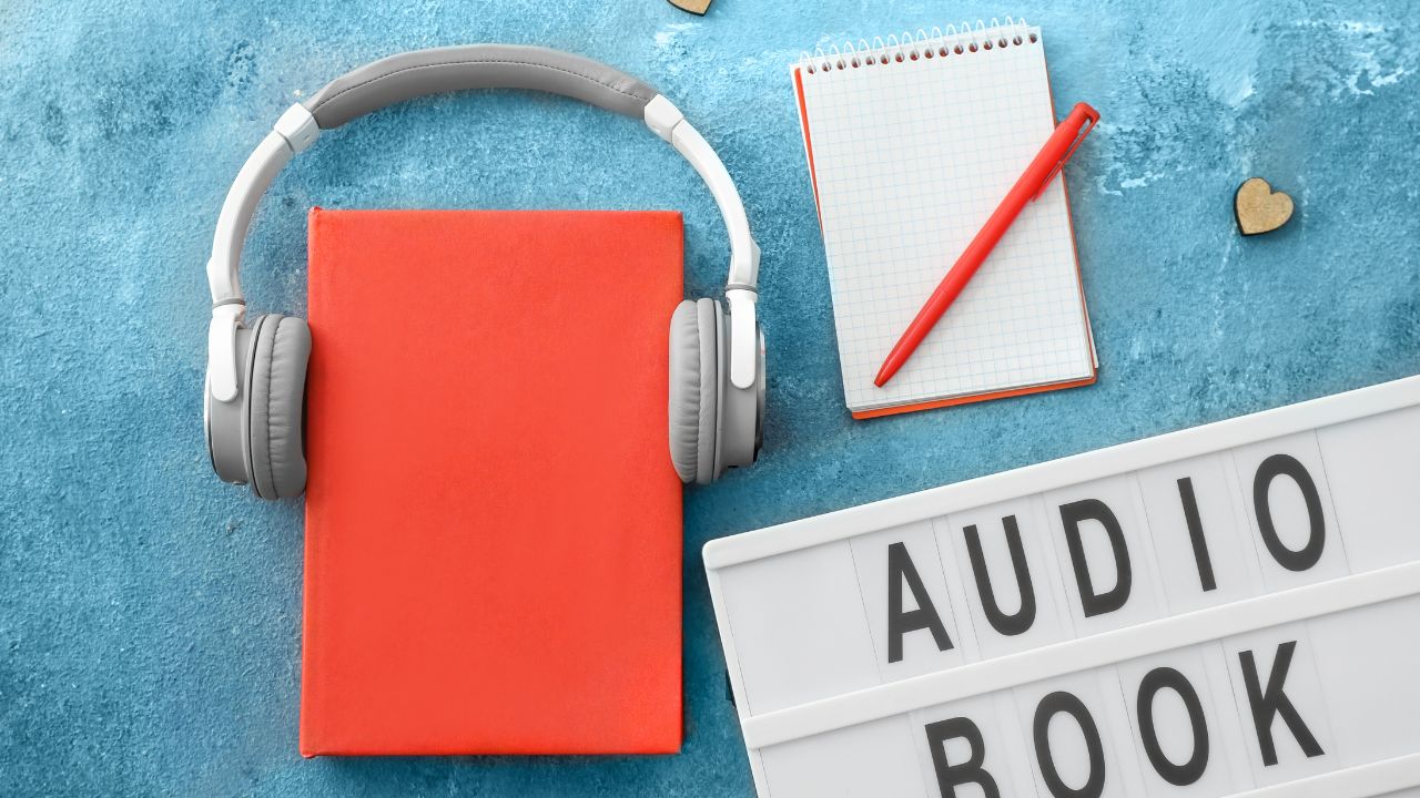 Libro, auriculares, cuaderno y cartel de audiolibro.