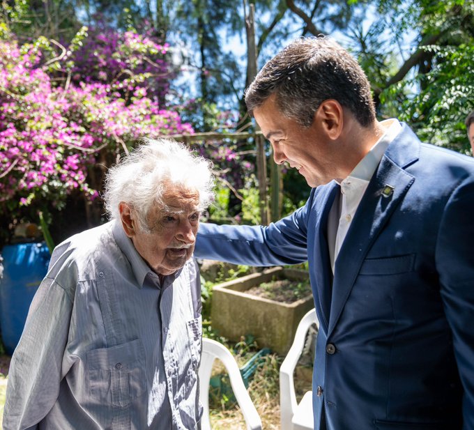 Dos hombres conversando en un jardín soleado.