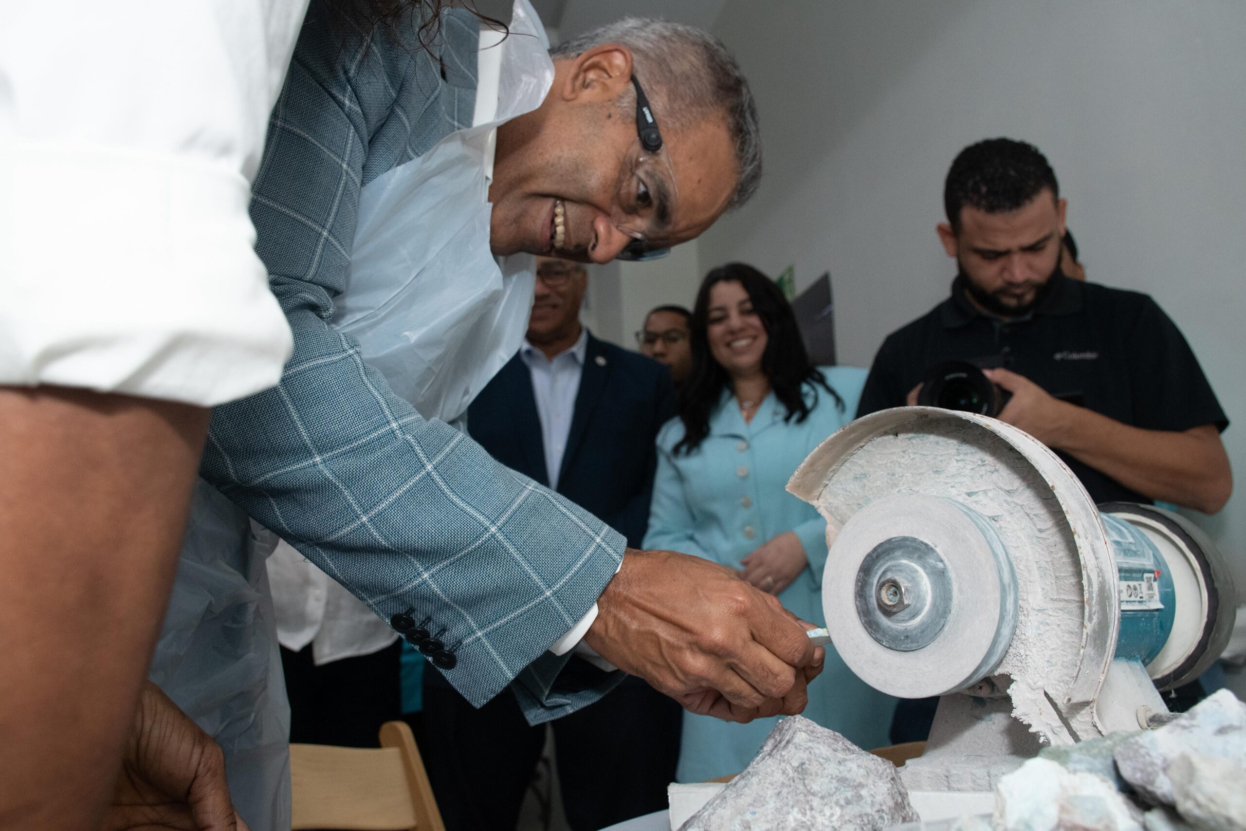 Persona usando máquina pulidora, rodeada de gente.