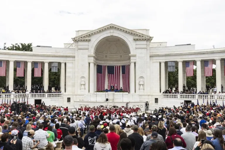 Ceremonia multitudinaria en edificio con banderas estadounidenses.