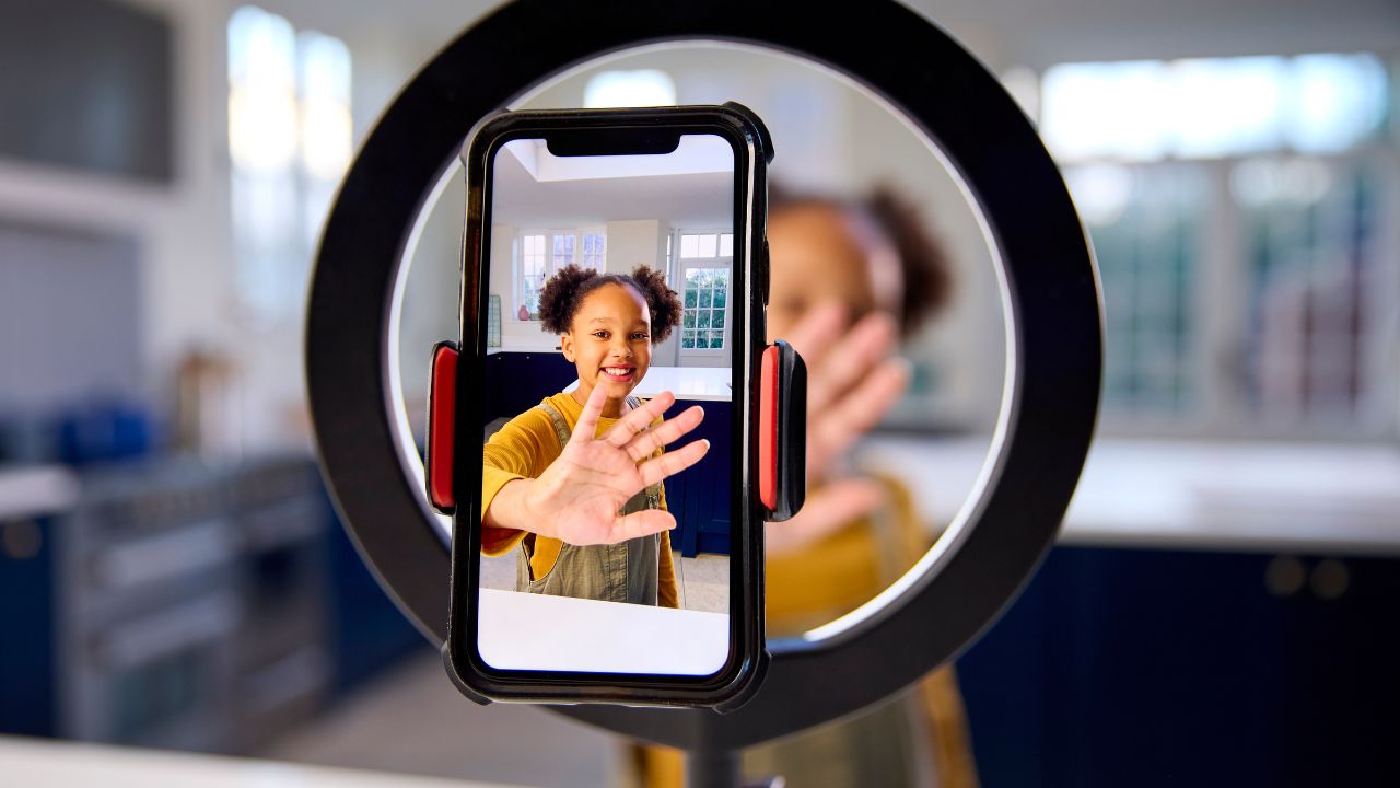 Niña sonriente grabando video con luz anular y móvil