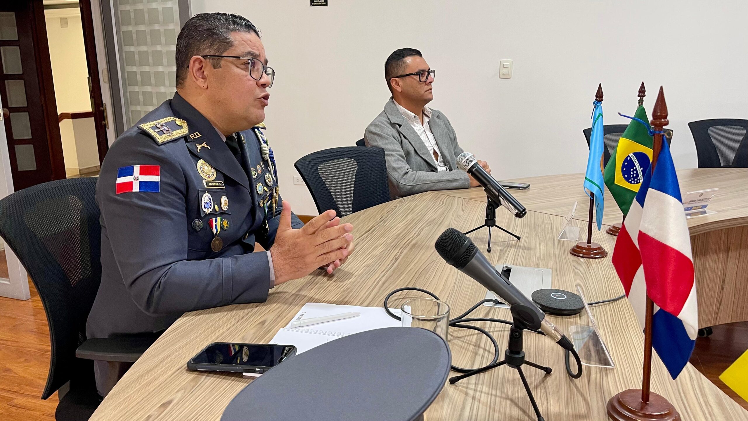 Reunión oficial con oficiales y banderas en mesa.