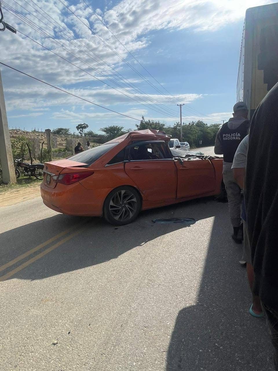 Accidente de coche naranja en carretera con policía presente.