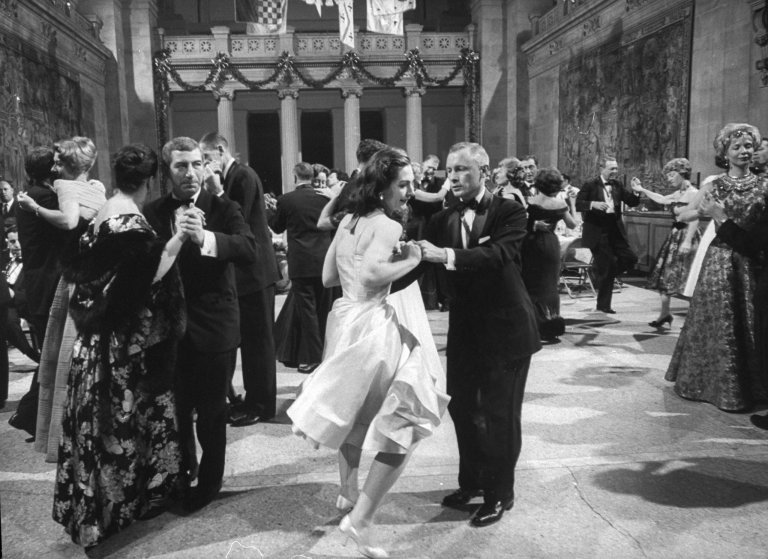 Baile de gala en un salón elegante, parejas bailando.