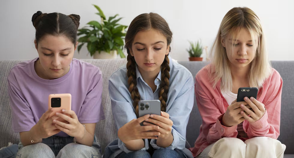 Tres chicas usando móviles en un sofá