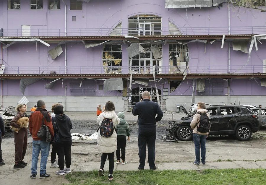 Personas observan edificio dañado, coches quemados.
