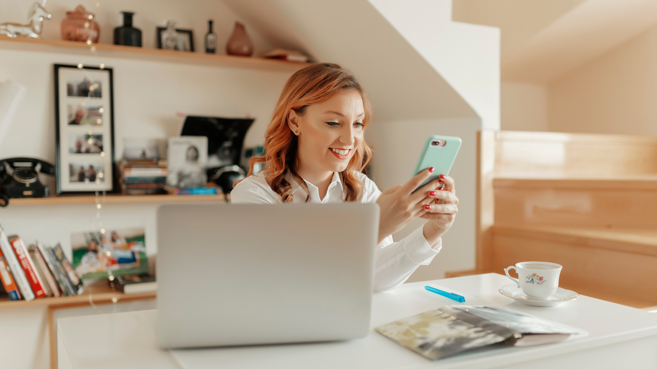 Mujer sonriendo mientras usa su teléfono en oficina.