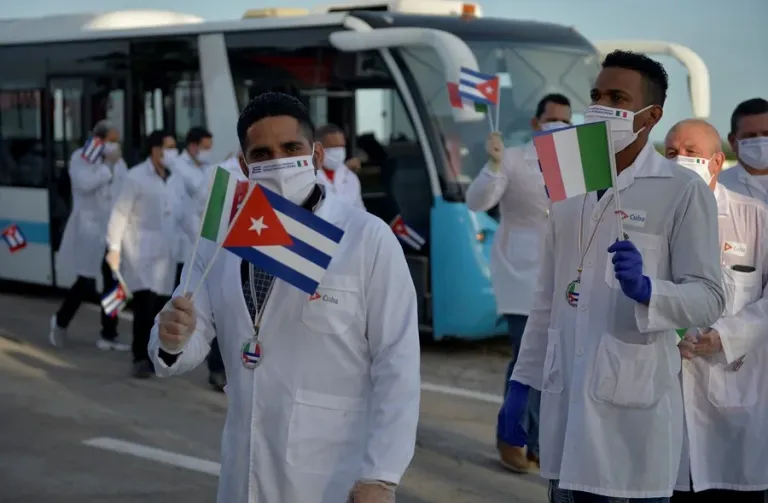 Médicos cubanos con banderas, autobús al fondo.