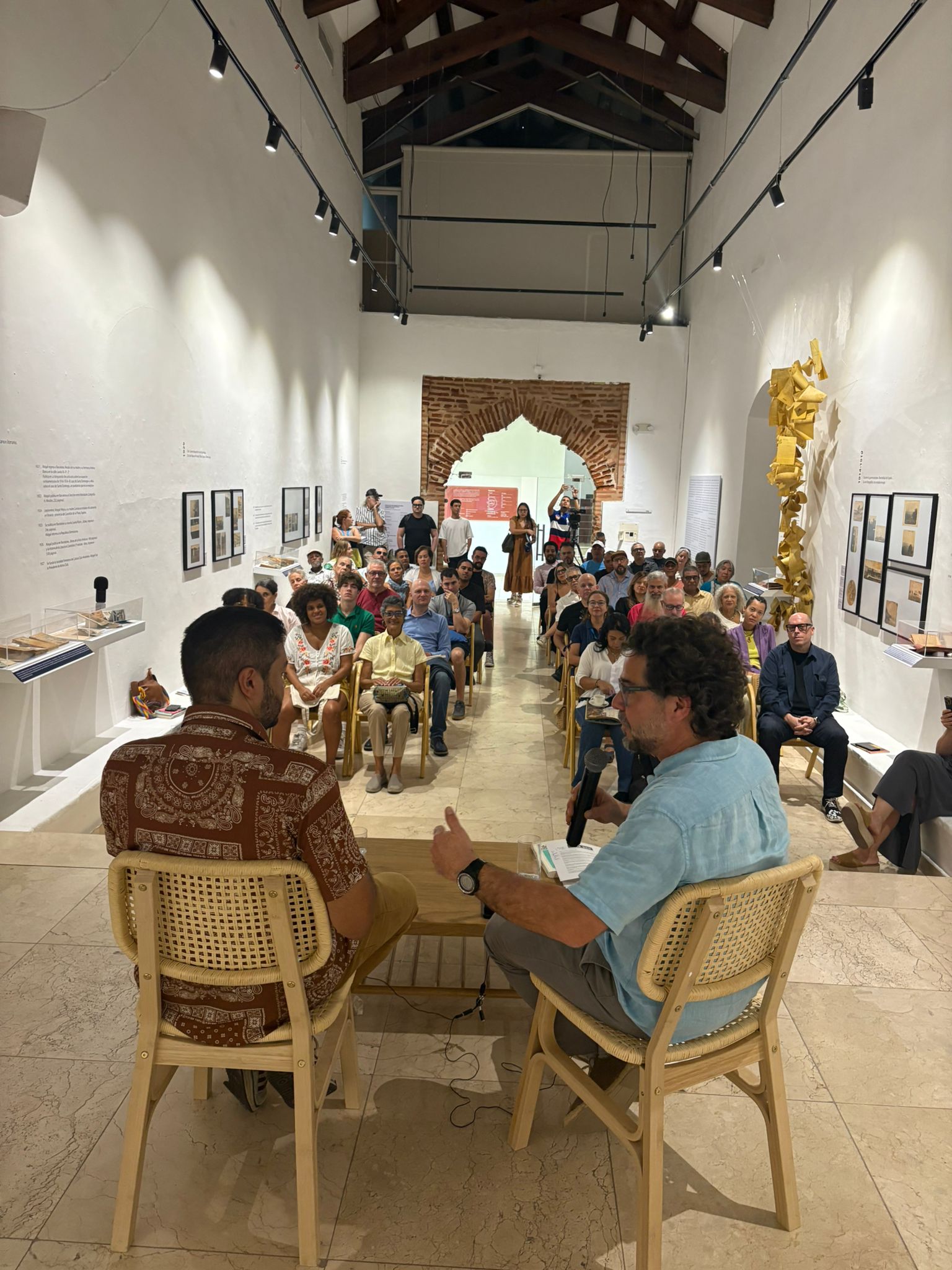 Charla en sala con público atento y decoración artística.