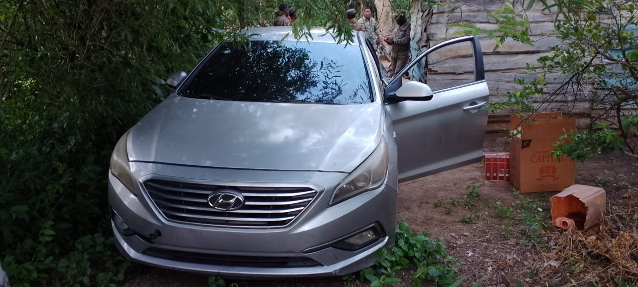 Coche plateado aparcado entre árboles y cajas.