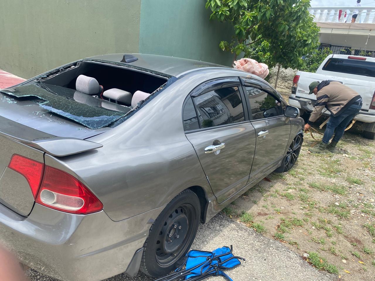 Coche con ventana trasera rota, hombre reparando rueda