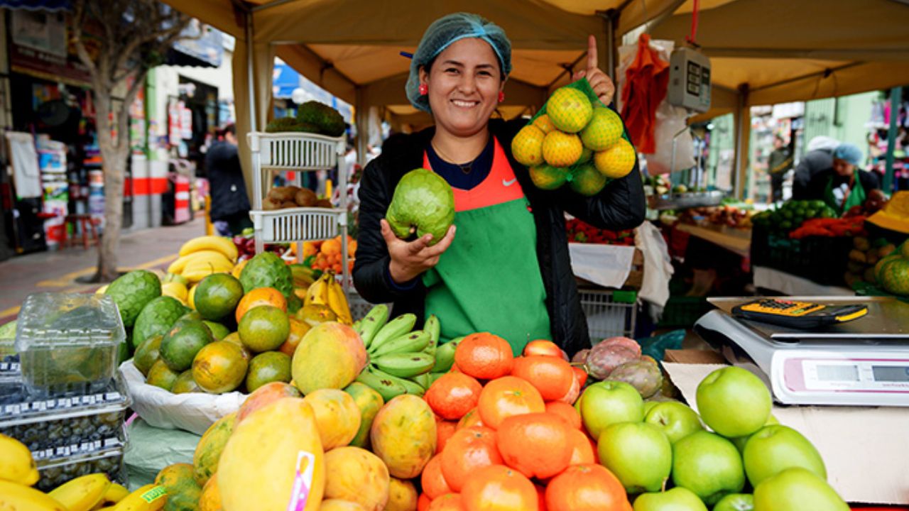Vendedora sonriendo en mercado de frutas variadas.
