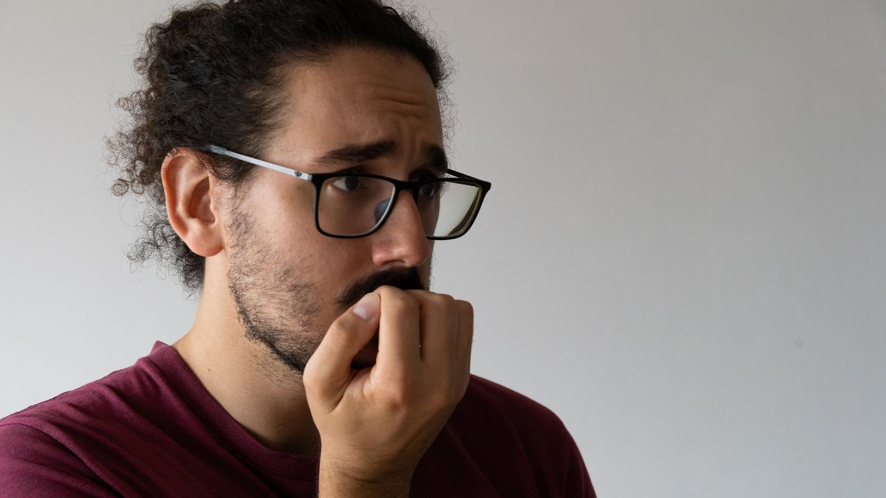 Hombre con gafas, preocupado y mordiendo uñas