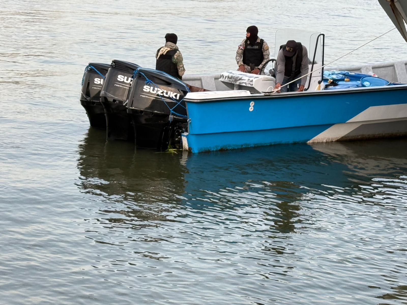 Barco azul en el agua con tres personas a bordo.