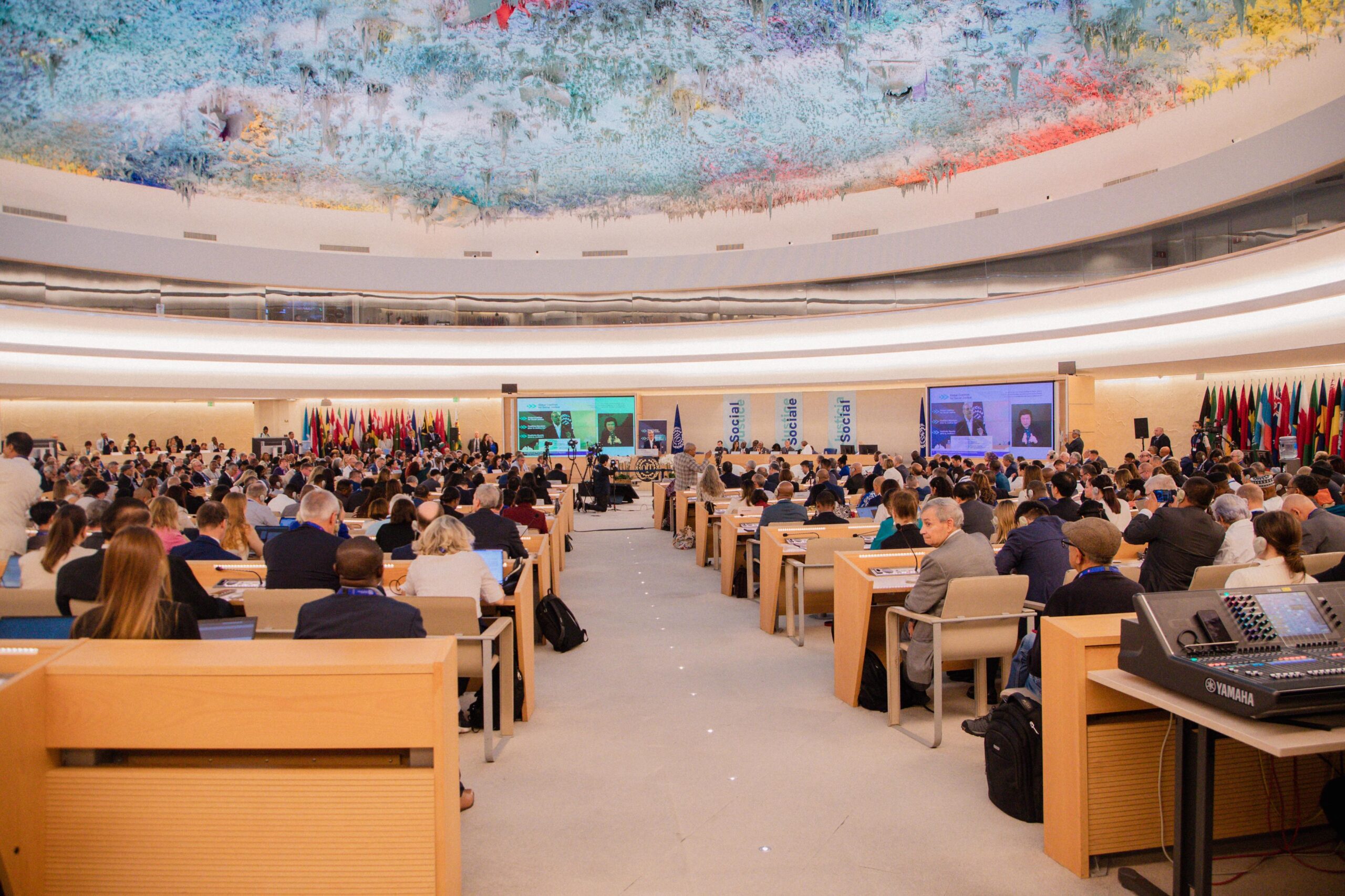 Reunión internacional en sala con asistentes y banderas.