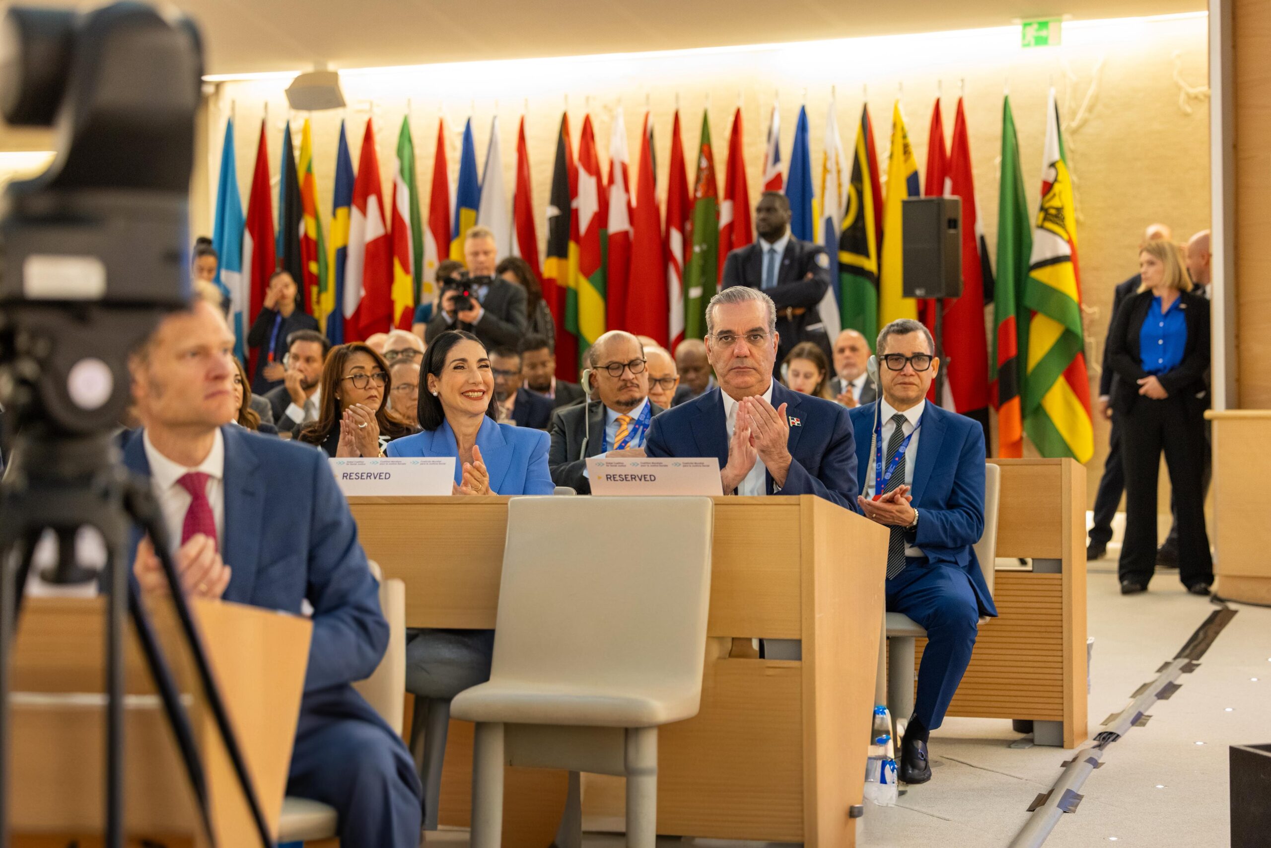 Personas aplaudiendo en conferencia internacional con banderas.