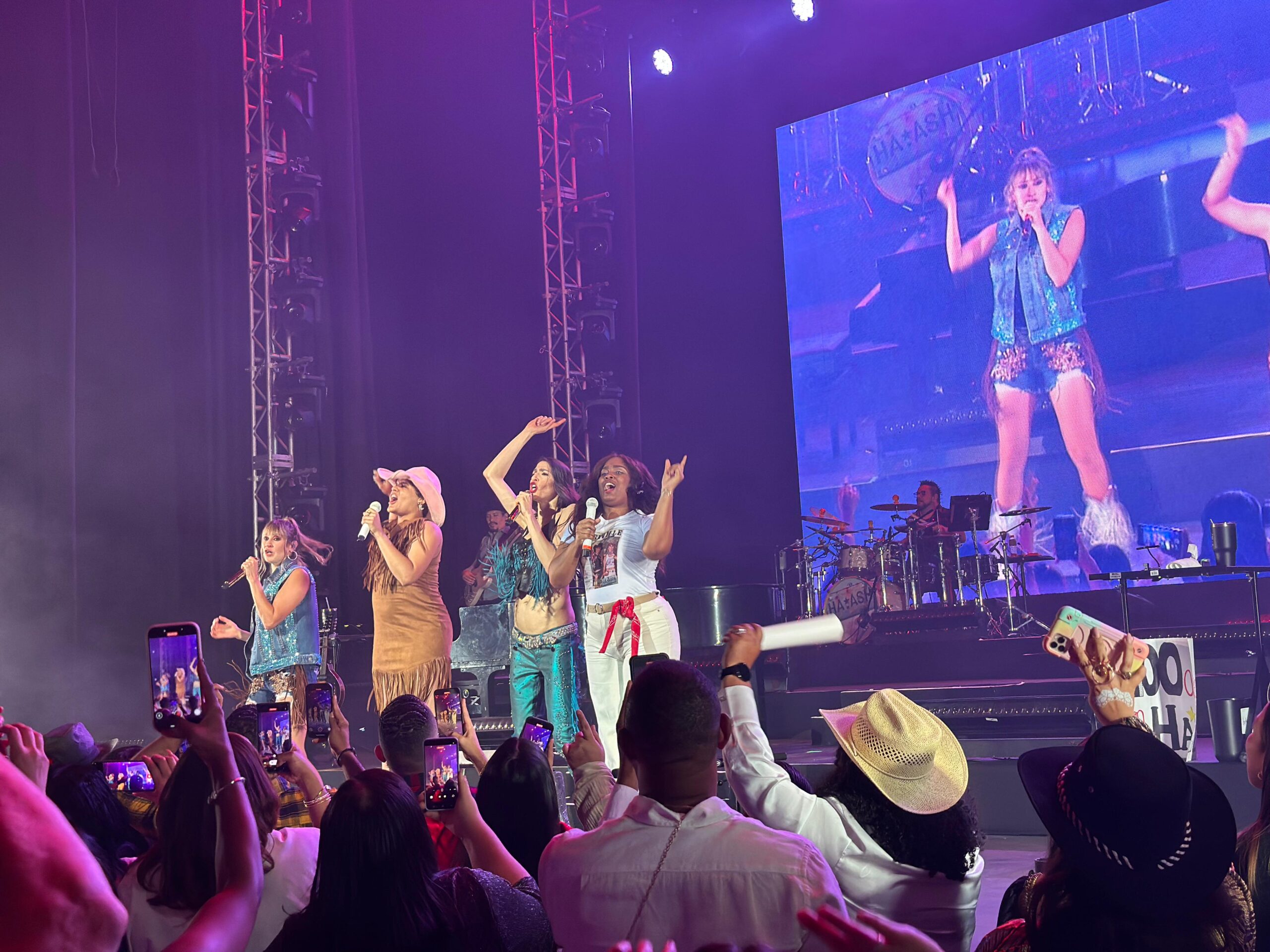 Concierto con cantantes en escenario y gran pantalla.