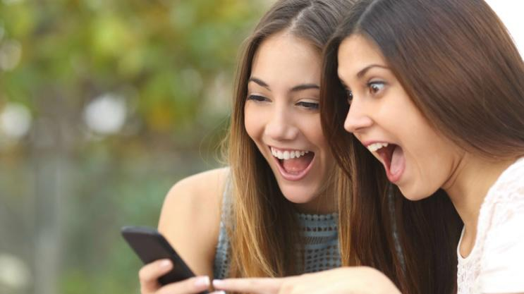 Dos mujeres sorprendidas mirando móvil.