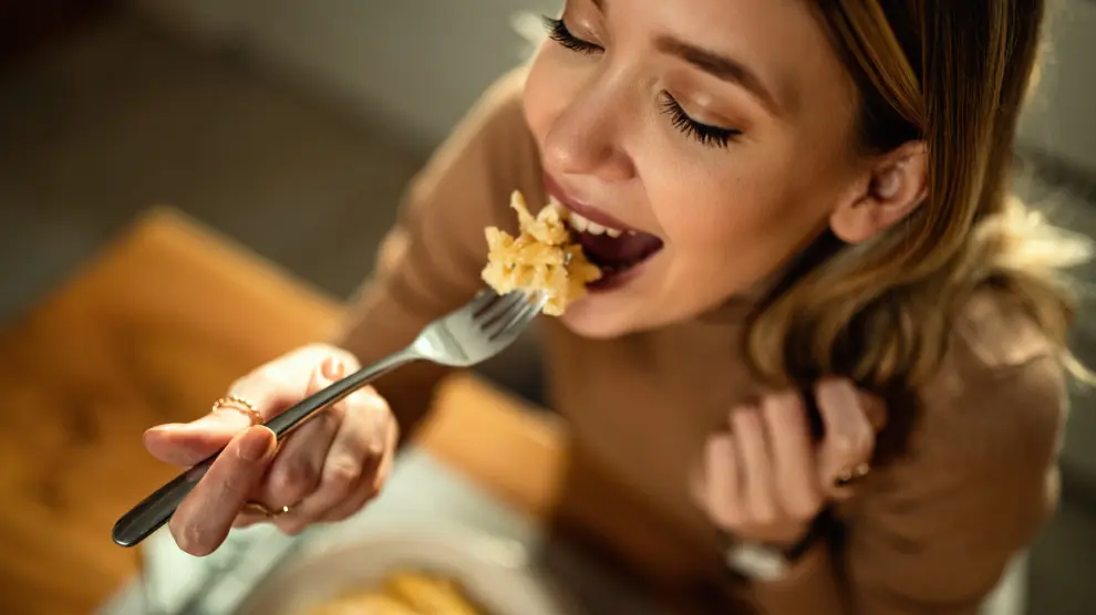 Mujer sonriendo comiendo pasta con tenedor.
