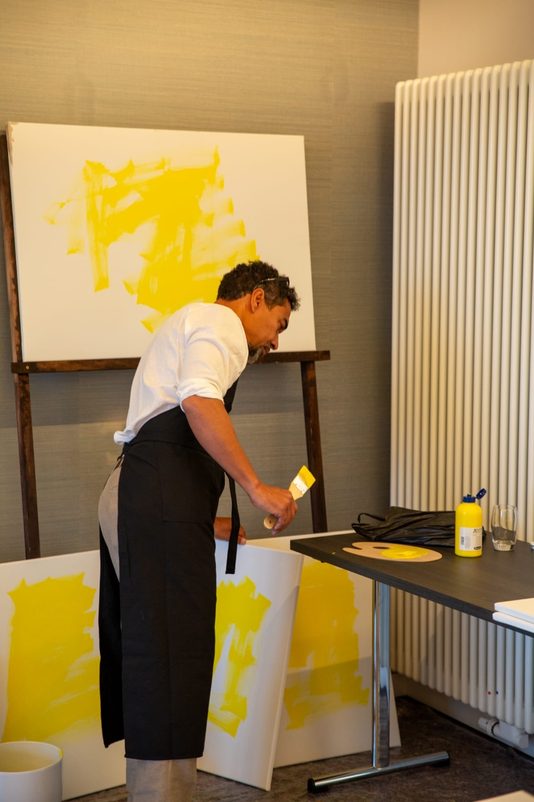 Artista pinta lienzo amarillo con pincel grande.