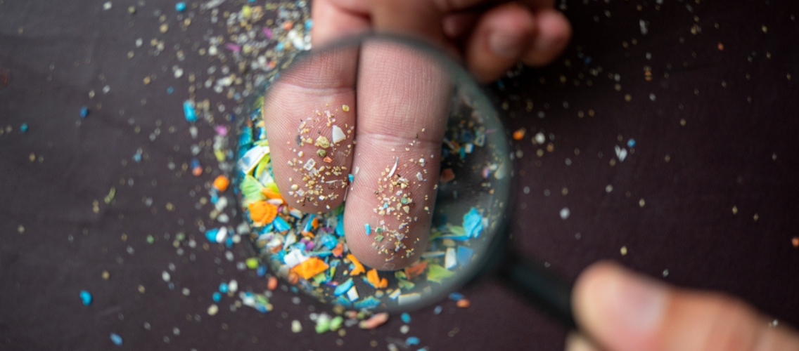 Lupa observando microplásticos sobre dedos.