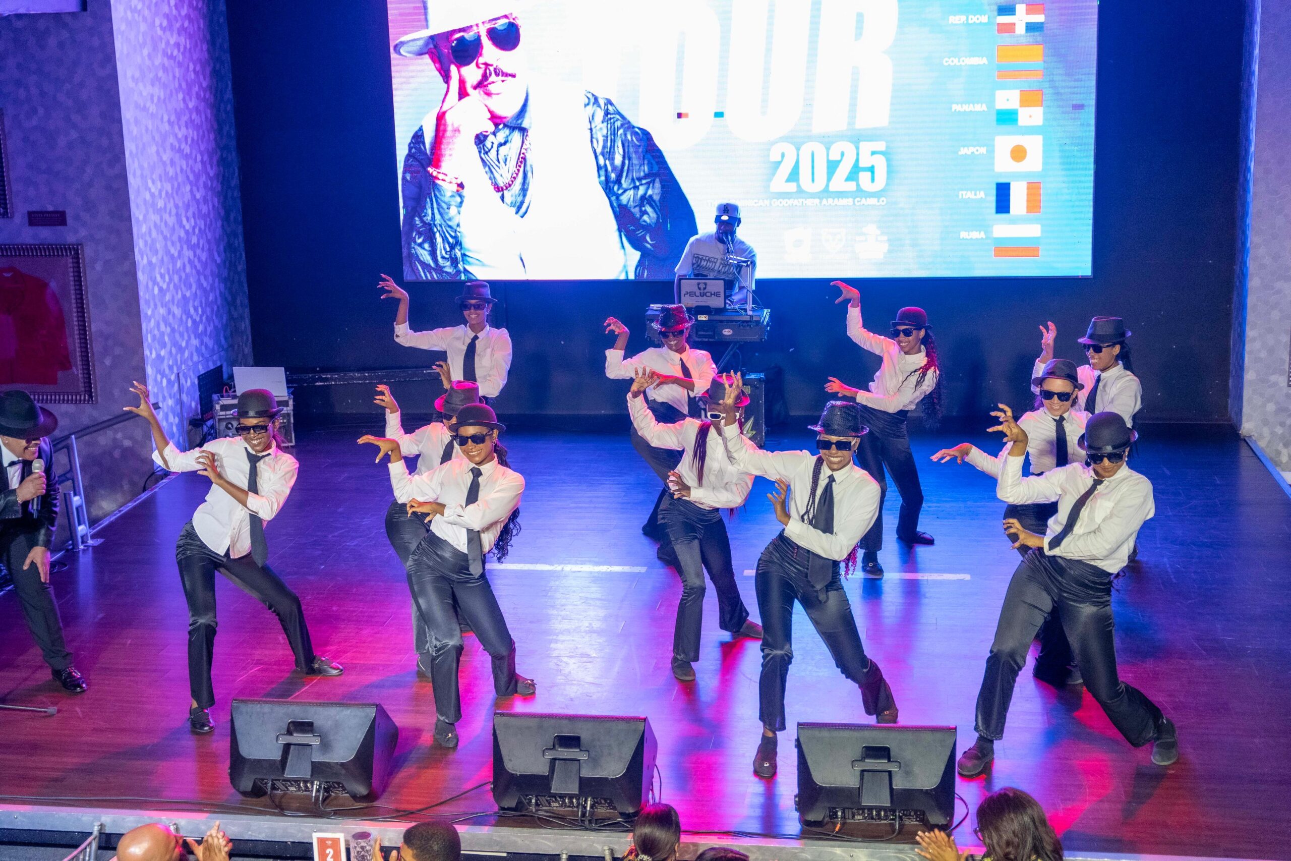 Grupo de bailarines actuando en escenario con pantalla grande.