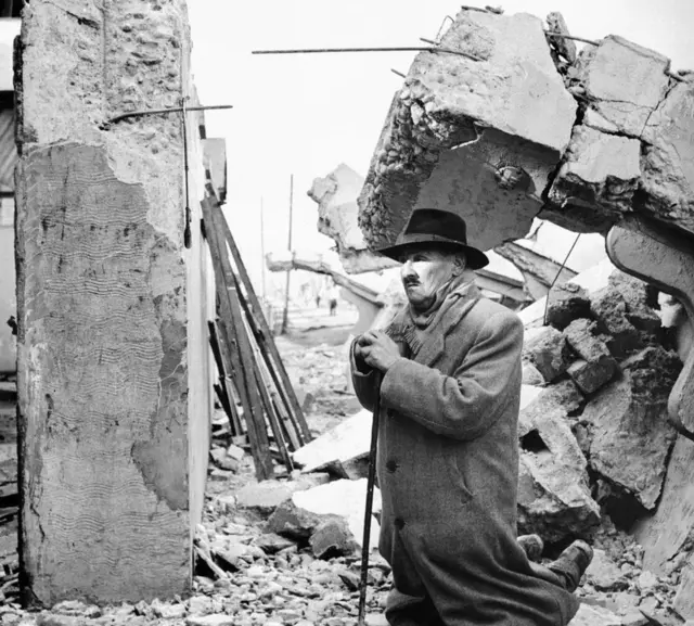Hombre entre escombros de edificio demolido.