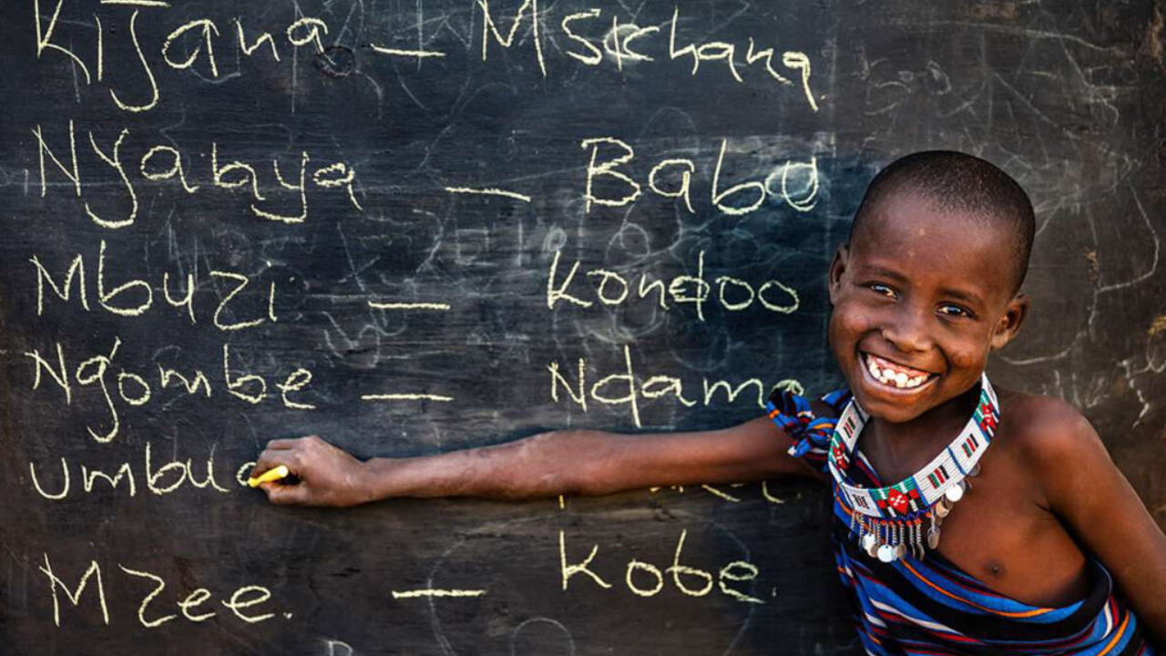 Niño escribiendo en pizarra sonriente con tiza amarilla.