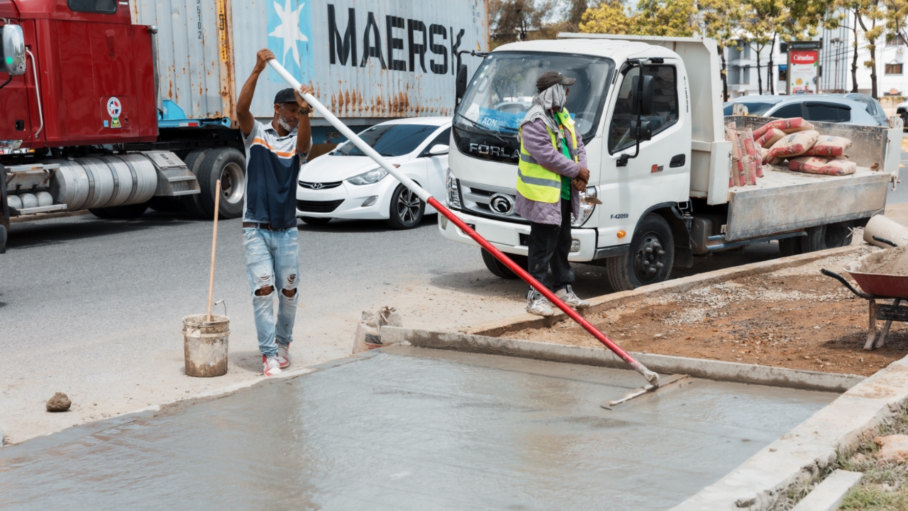 Trabajadores construyendo acera de concreto en la calle.