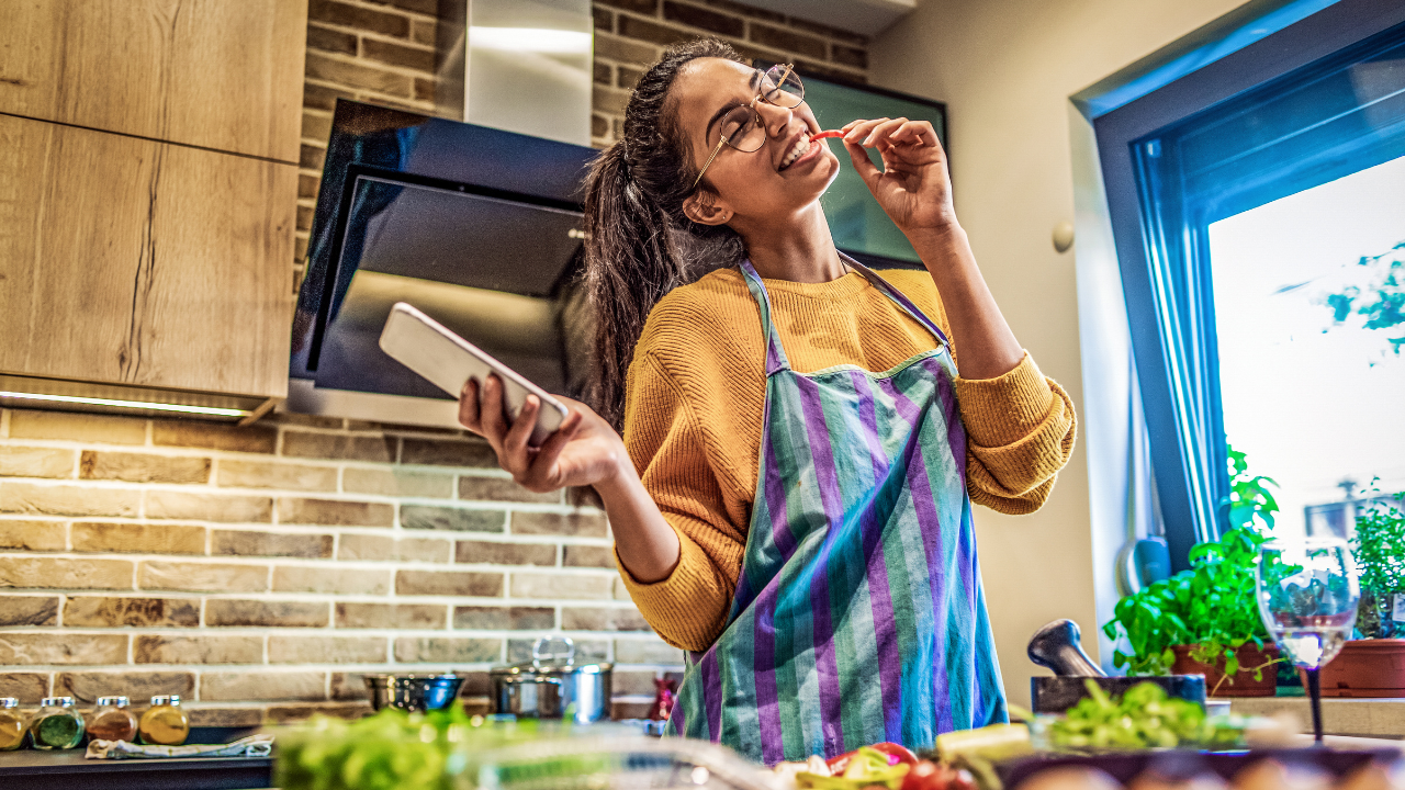 Persona cocinando alegremente con móvil en cocina moderna.
