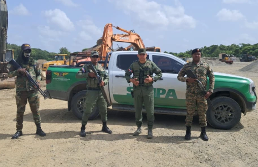 Guardias armados junto a vehículo y excavadora.