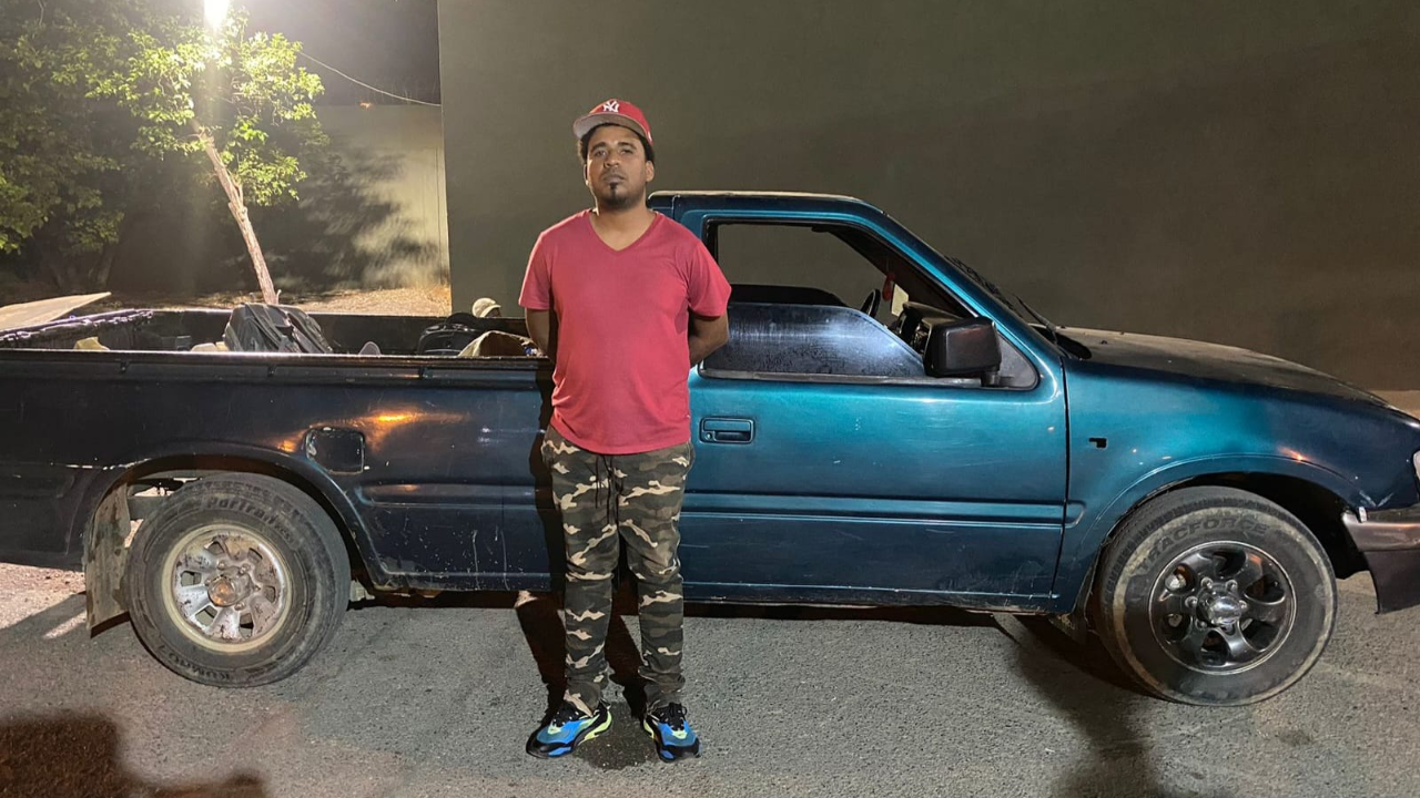 Hombre con gorra junto a camioneta azul de noche