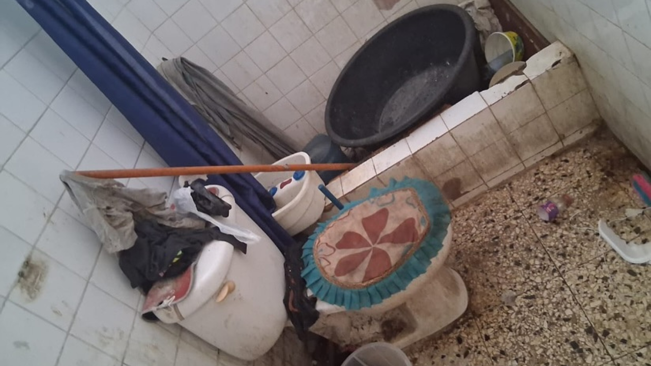 Baño sucio y desordenado con objetos esparcidos.