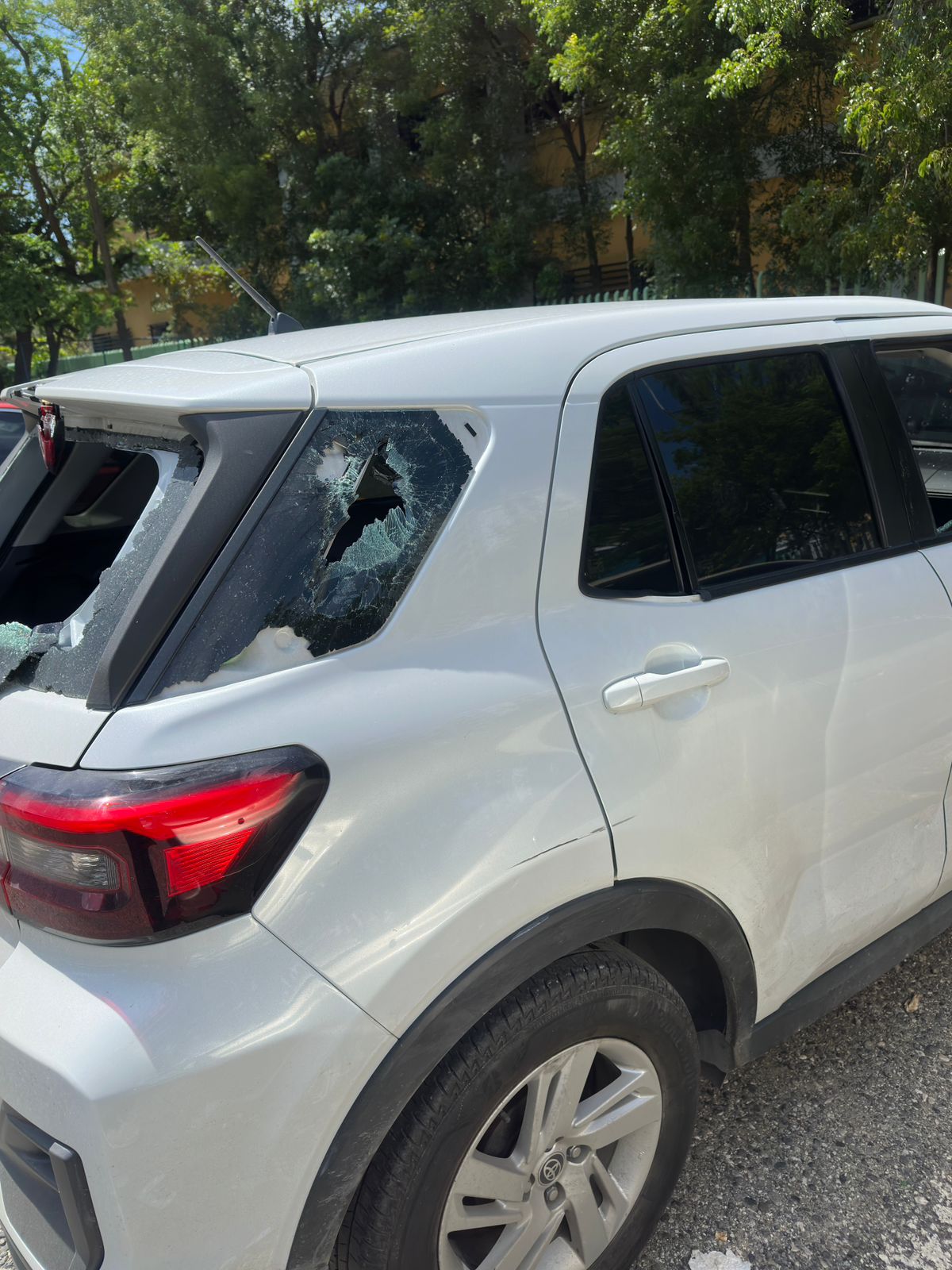 Coche blanco con ventana rota en el estacionamiento.