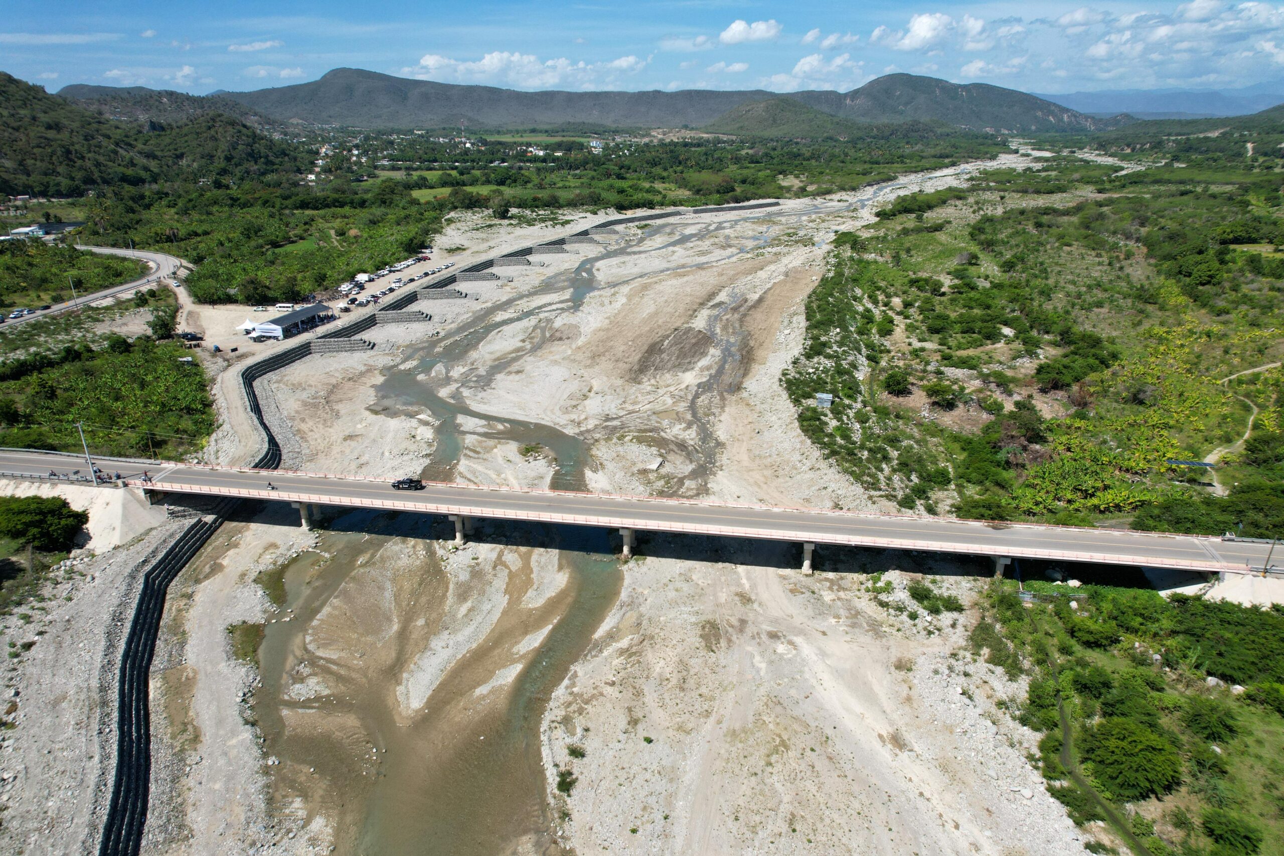 Puente sobre río con escasa agua y vegetación alrededor.