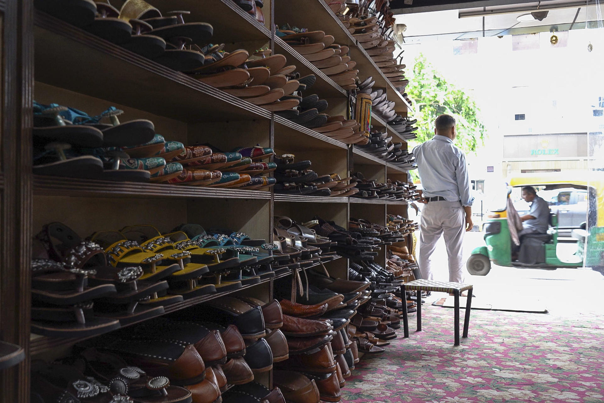 Tienda de zapatos con sandalias exhibidas, tuk-tuk afuera.
