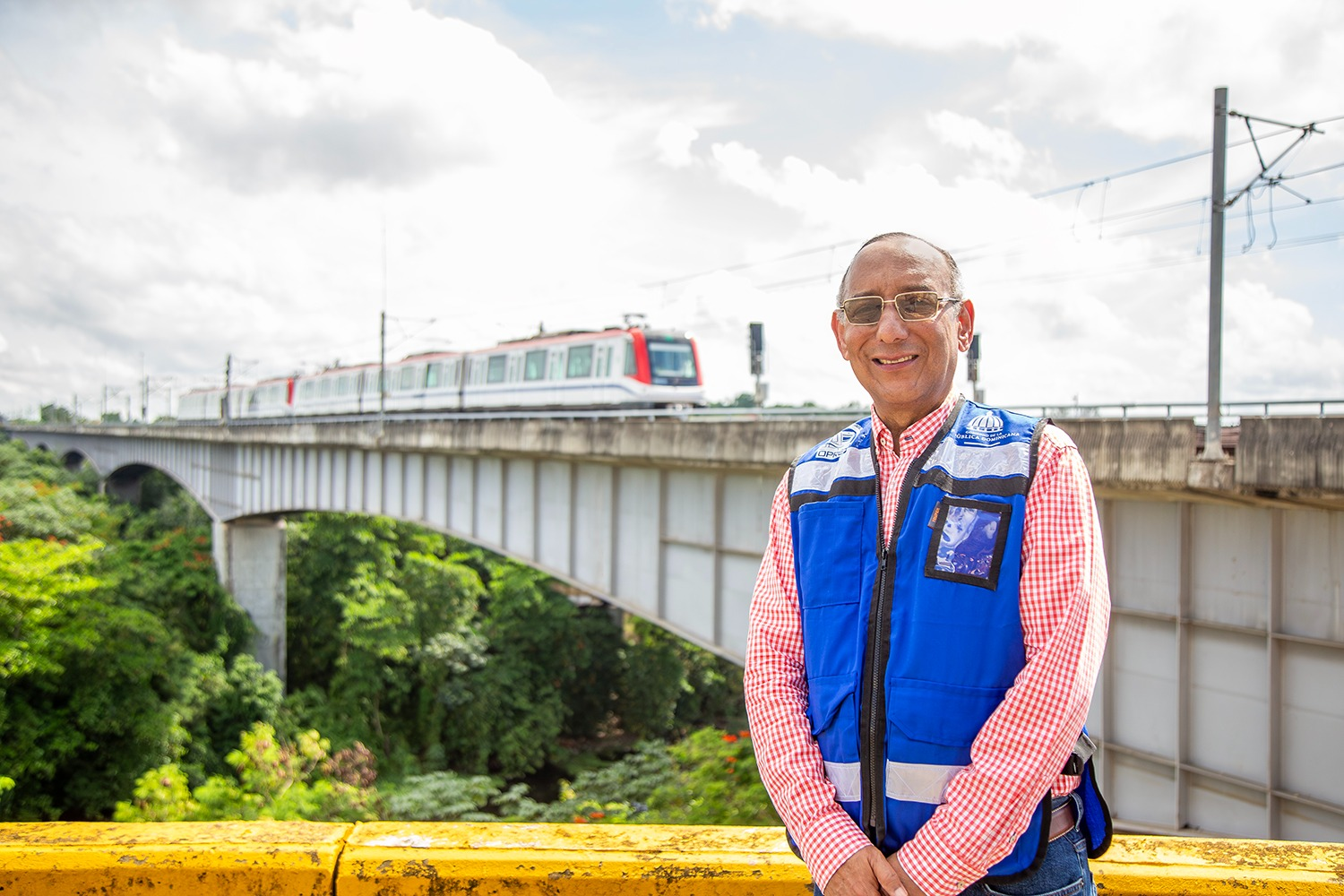 Hombre sonriente frente a tren en puente.