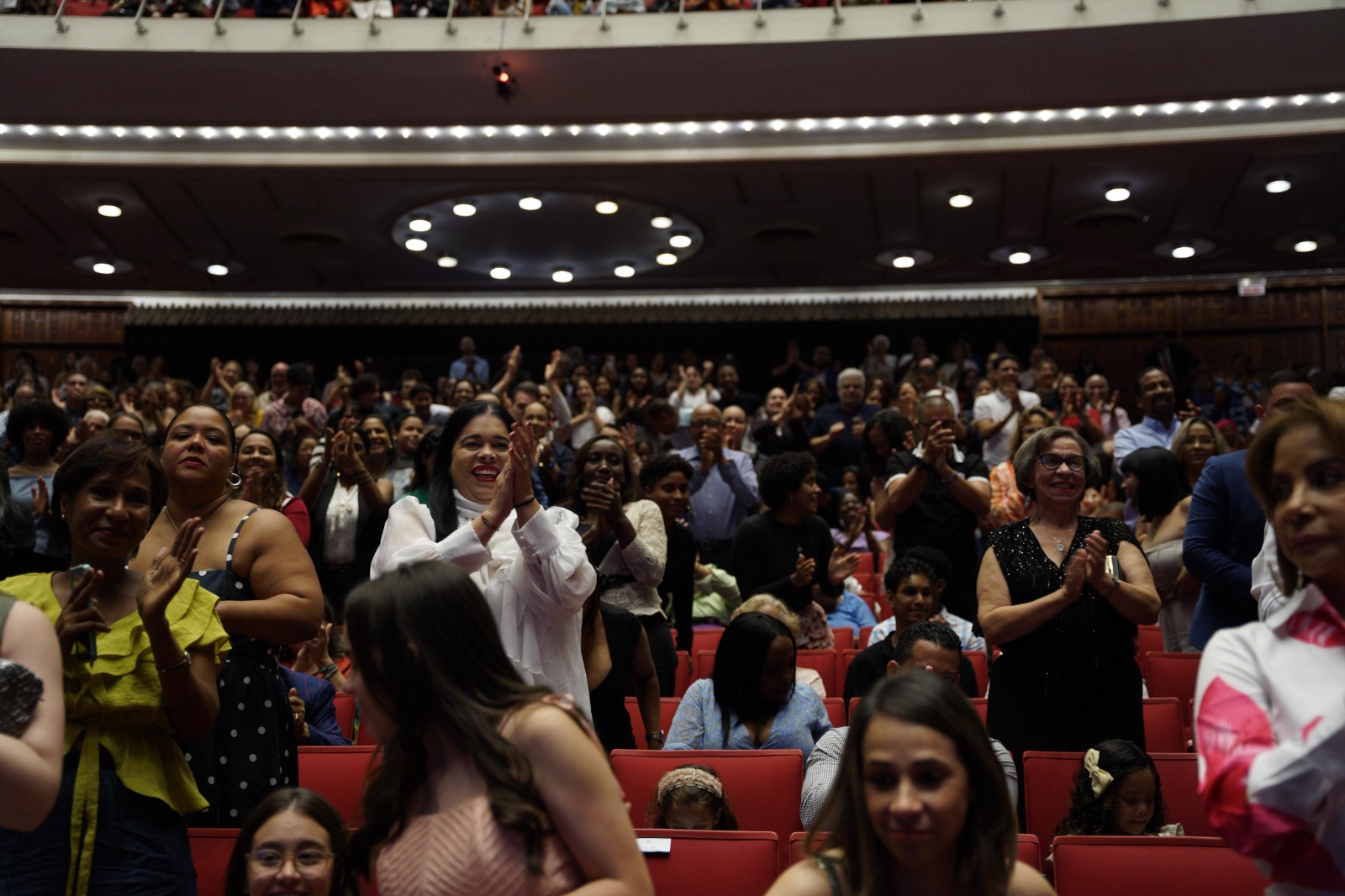 Público aplaudiendo de pie en un teatro lleno.