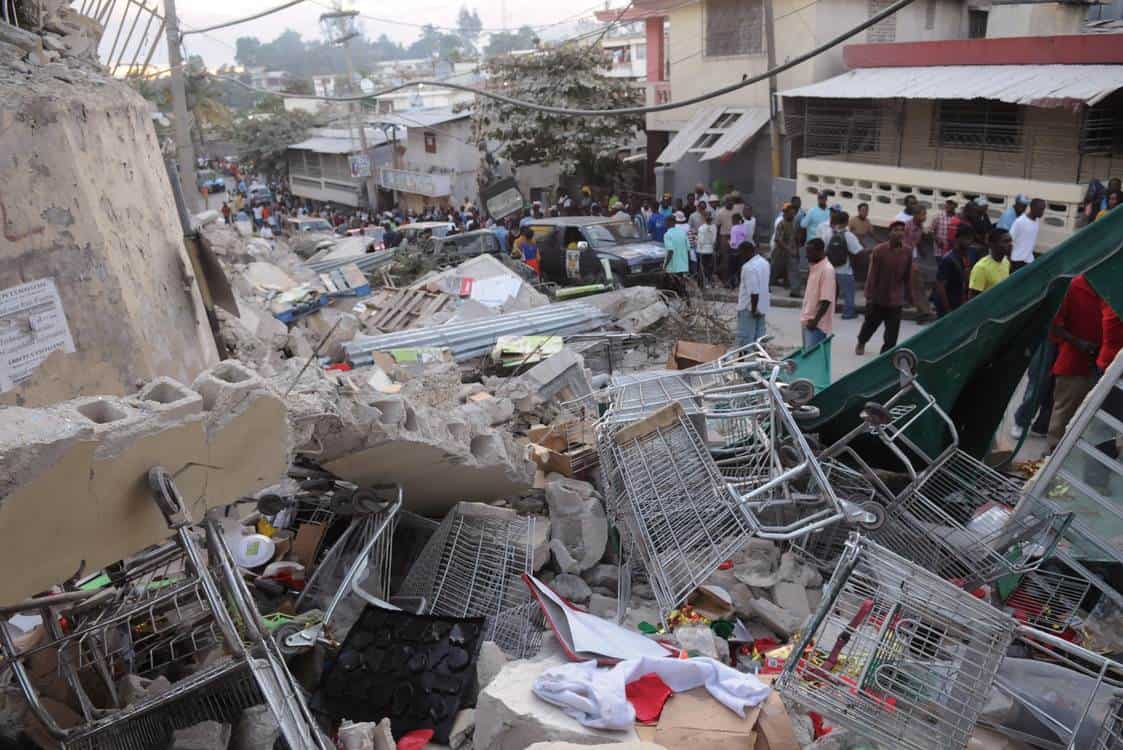 Escombros en calle tras terremoto, personas observan.